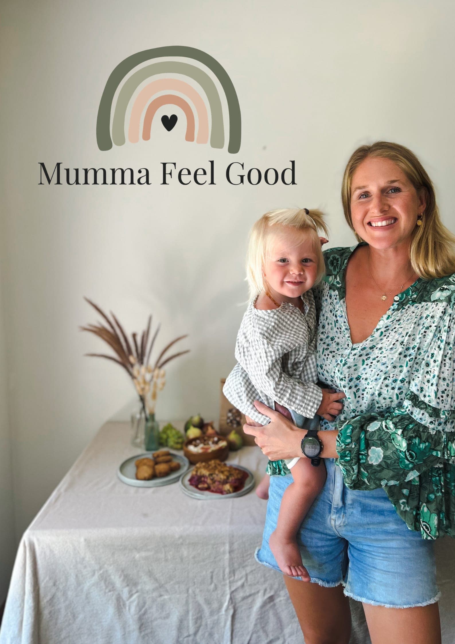 Grace holding her daughter beside a table of Mumma Feel Good food.
